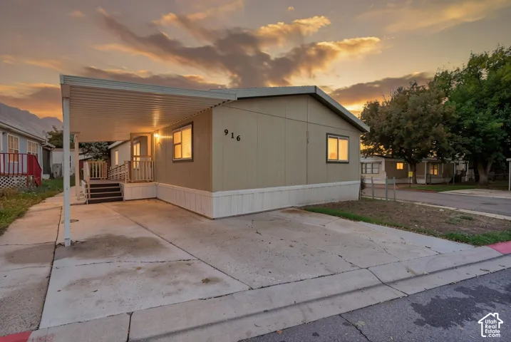 Single-level exterior featuring neutral-toned siding, a concrete driveway, an attached carport, and a raised entry platform with metal railings
