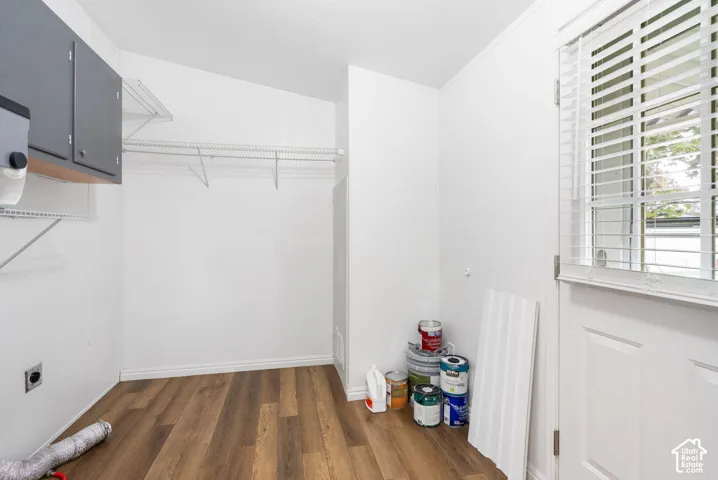 Utility area featuring wood-finish flooring, wall-mounted cabinetry, white wire shelving, and an exterior door with integrated blinds