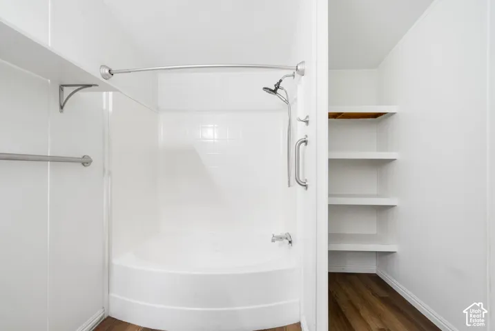 Built-in soaking tub with a shower head, curved shower rod, metal grab bar, and integrated white shelving