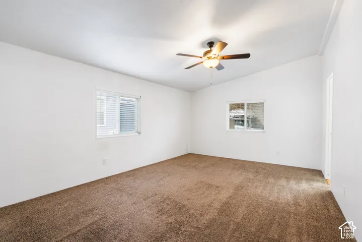 Neutral interior space featuring high-angled ceilings, plush carpeting, dual windows with integrated blinds, and a centrally mounted ceiling fan with light fixture