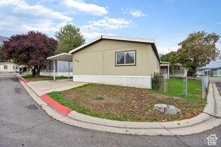 Exterior featuring a covered carport, chain-link fencing, and mature trees
