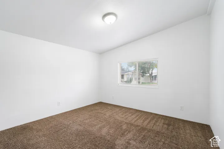 Room featuring neutral-toned carpeting, a vaulted ceiling, and a flush-mount light fixture