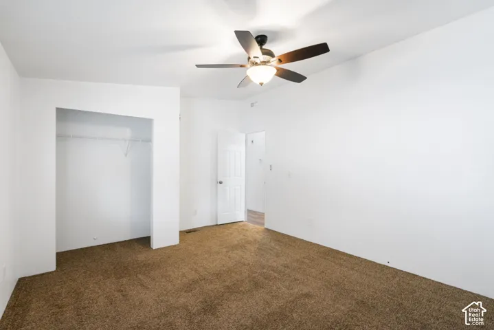 Neutral interior space featuring carpeted flooring, a ceiling fan with integrated lighting, and a closet with built-in shelving