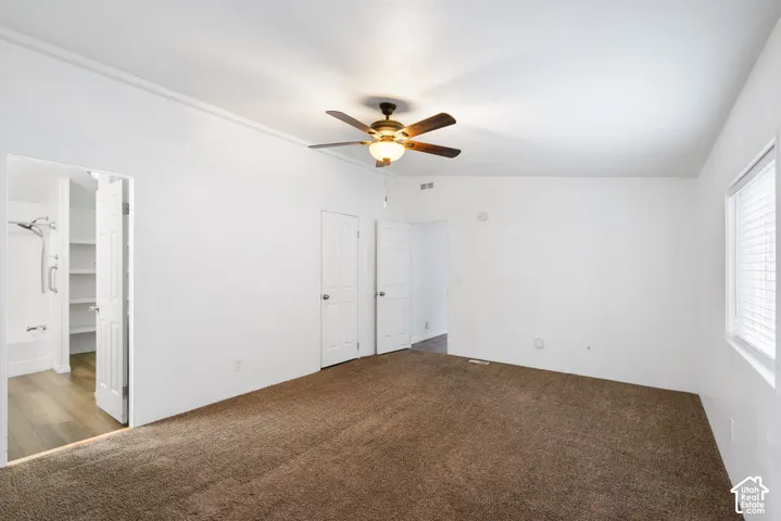 Neutral-toned carpeting, vaulted ceilings, multi-blade ceiling fan with central lighting, and two interior doors with hardware