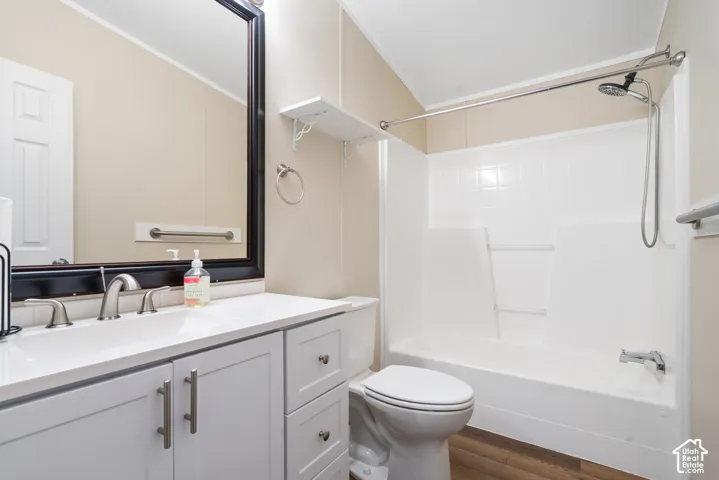 Bathroom featuring a vanity with light-toned cabinetry, solid-surface countertop, and an integrated basin, paired with a white tub-shower combination, metallic fixtures, and wood-finish flooring