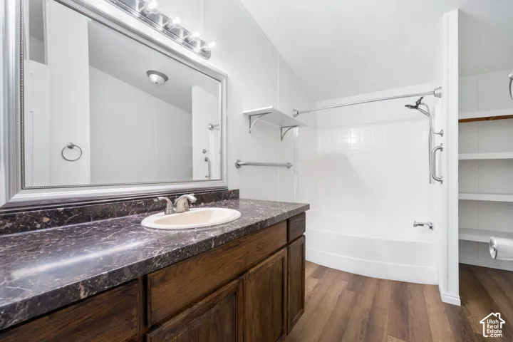 Bathroom featuring dark-finish wood cabinetry, a dark stone-patterned countertop with an integrated oval sink, wood-finish flooring, and a tub-shower combination with white surround tile