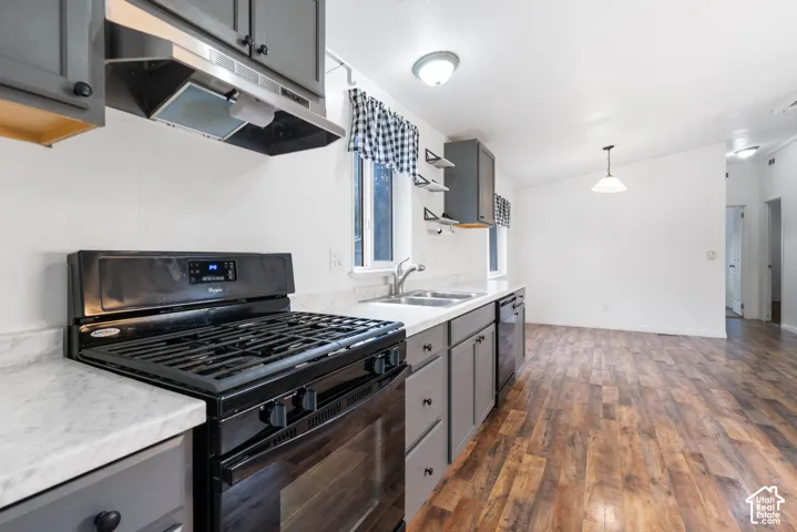 Kitchen featuring charcoal-toned cabinetry, light-toned stone-finish countertops, black gas range, stainless steel dual-basin sink, and wood-finish flooring
