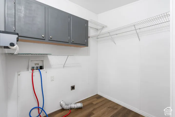 Utility room featuring wood-finish flooring, dark grey wall-mounted cabinetry, and dual wire shelving systems