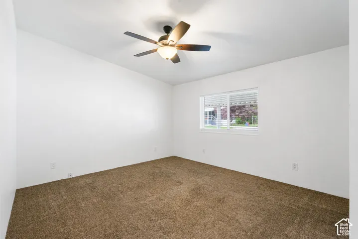 Neutral-toned wall-to-wall carpeting, ceiling-mounted paddle fan with integrated lighting, and white walls featuring a sliding window