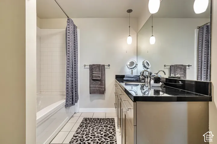 Bathroom featuring a vanity with dark countertop, large wall-to-wall mirror, two pendant light fixtures, and a tub-shower combination with white tile surround and tile flooring