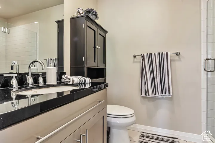Bathroom featuring a vanity with a dark stone countertop, undermount sink, chrome faucet, built-in dark wood cabinetry, and a glass-enclosed shower with tiled surround