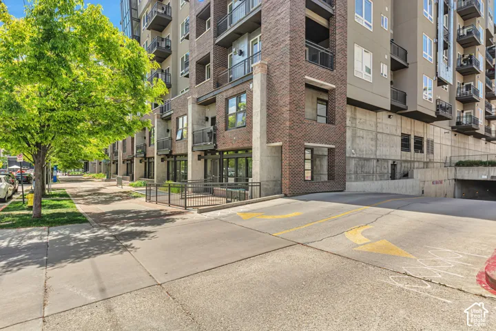 Multi-story building exterior featuring a masonry and smooth concrete facade, private metal-railed balconies, and a dedicated parking garage entrance