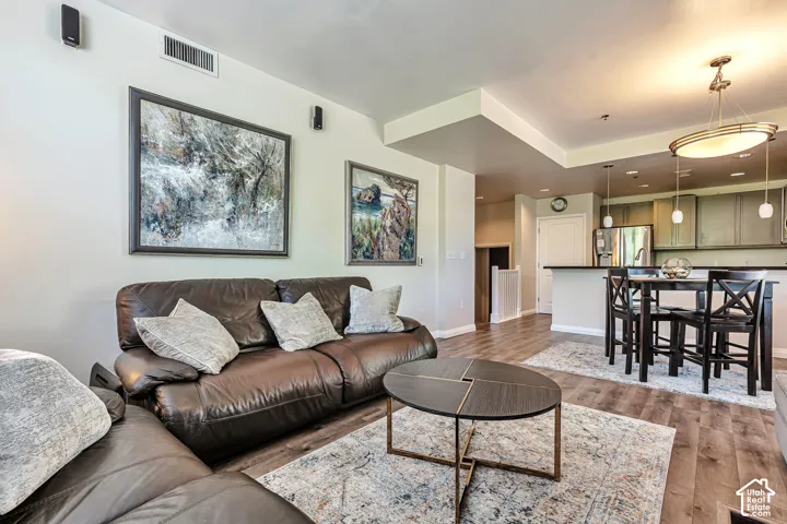 Open-concept interior featuring wood-finish flooring, recessed lighting, a kitchen breakfast bar, and a multi-tiered pendant light fixture