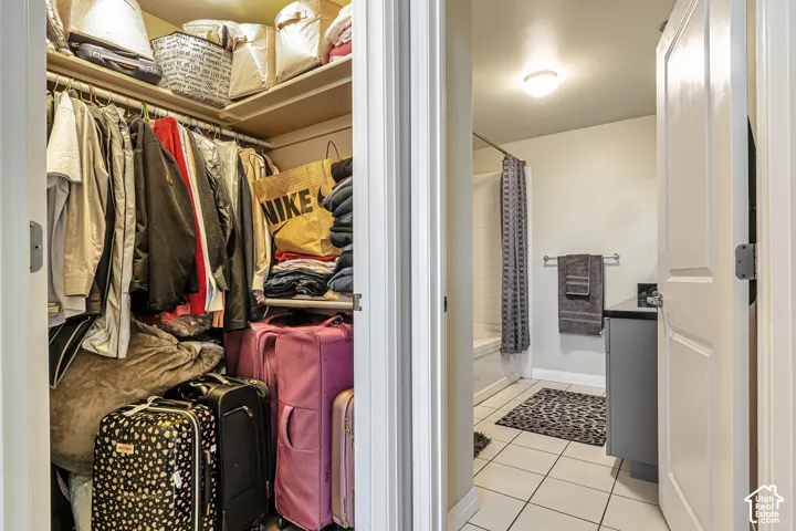Walk-in storage closet with built-in shelving, tile flooring, vanity with dark countertop, and shower-tub combination