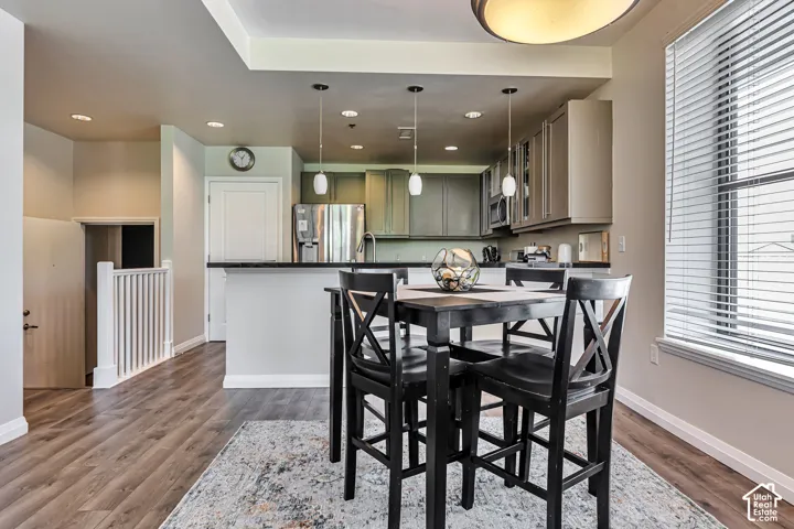Kitchen featuring cabinetry with a neutral finish, a breakfast bar with dark countertops, wood-finish flooring, recessed lighting, and pendant fixtures