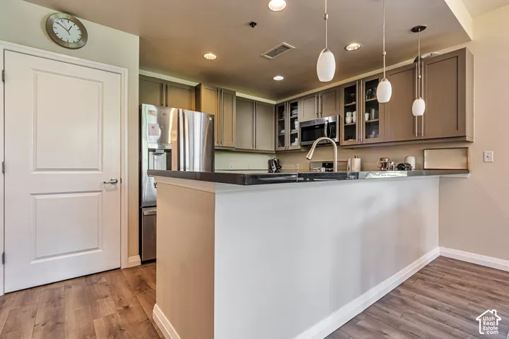 Kitchen featuring wood-finish flooring, shaker-style cabinetry, stainless steel appliances, dark stone-finish countertops, and pendant lighting