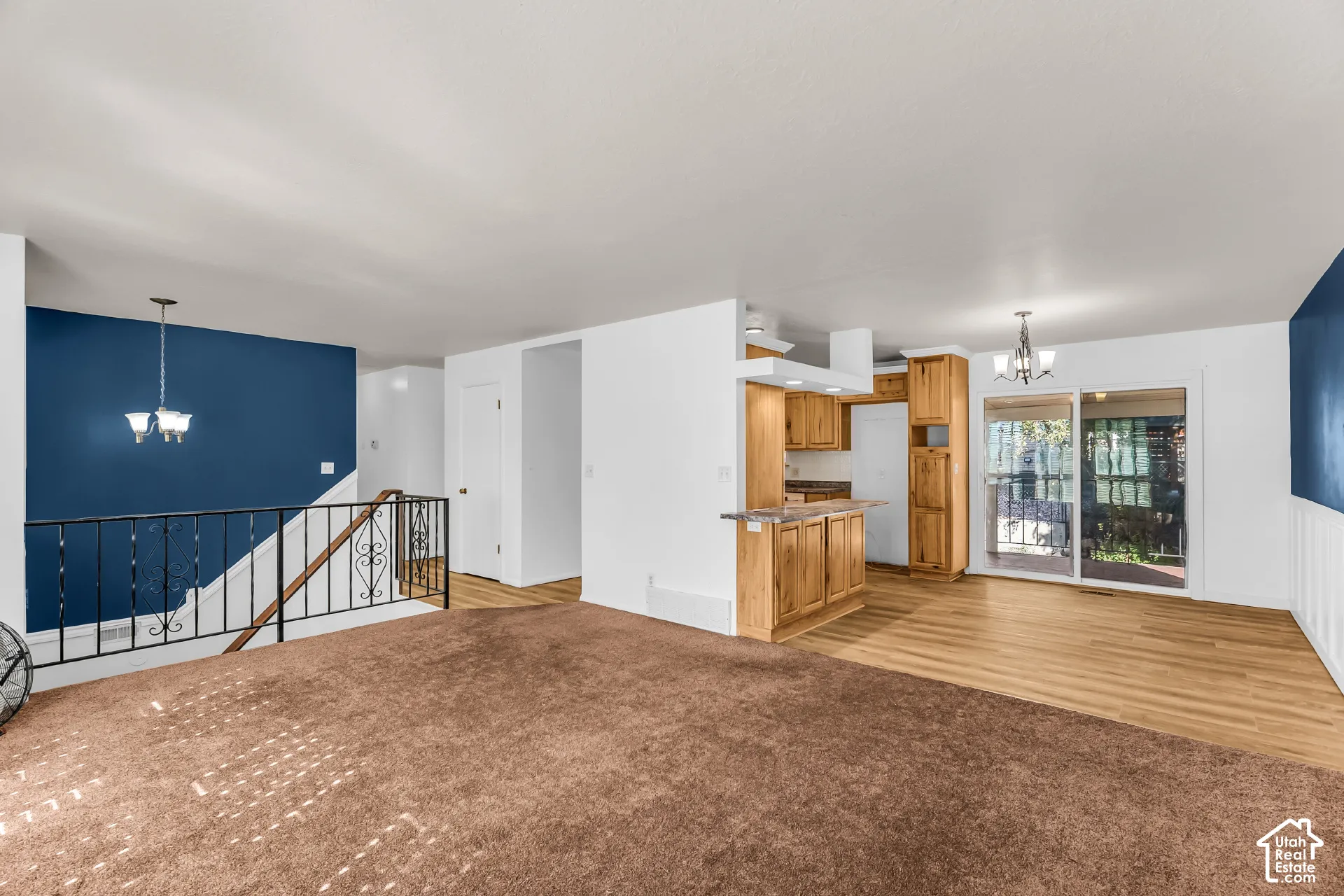 Open-concept interior featuring wood-finish cabinetry, hard surface flooring, decorative metal stair railing, and sliding glass doors