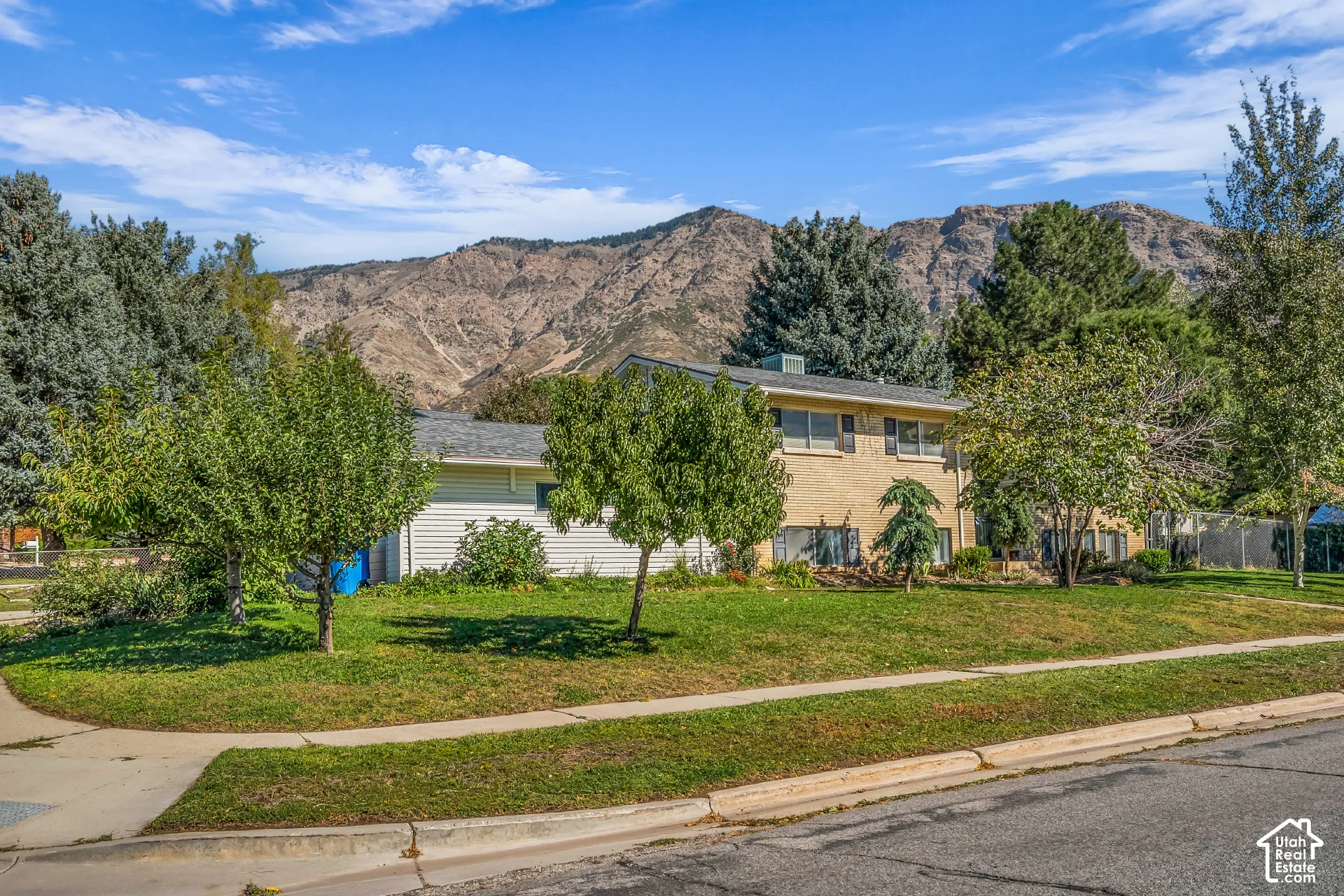 Split-level exterior featuring light brick and horizontal siding, set against a backdrop of mountain scenery, complemented by mature trees and a manicured lawn