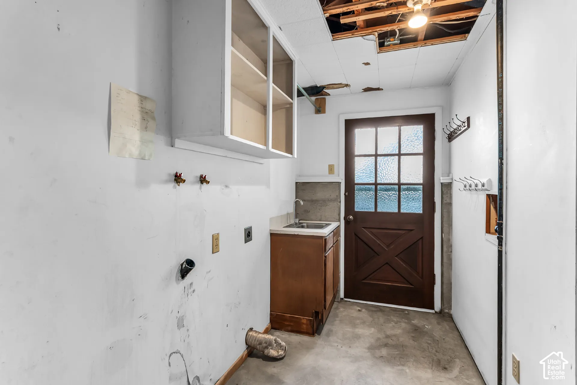 Utility room featuring an exterior door with textured glass, wall-mounted cabinetry, a built-in sink cabinet, and mounted wall hooks