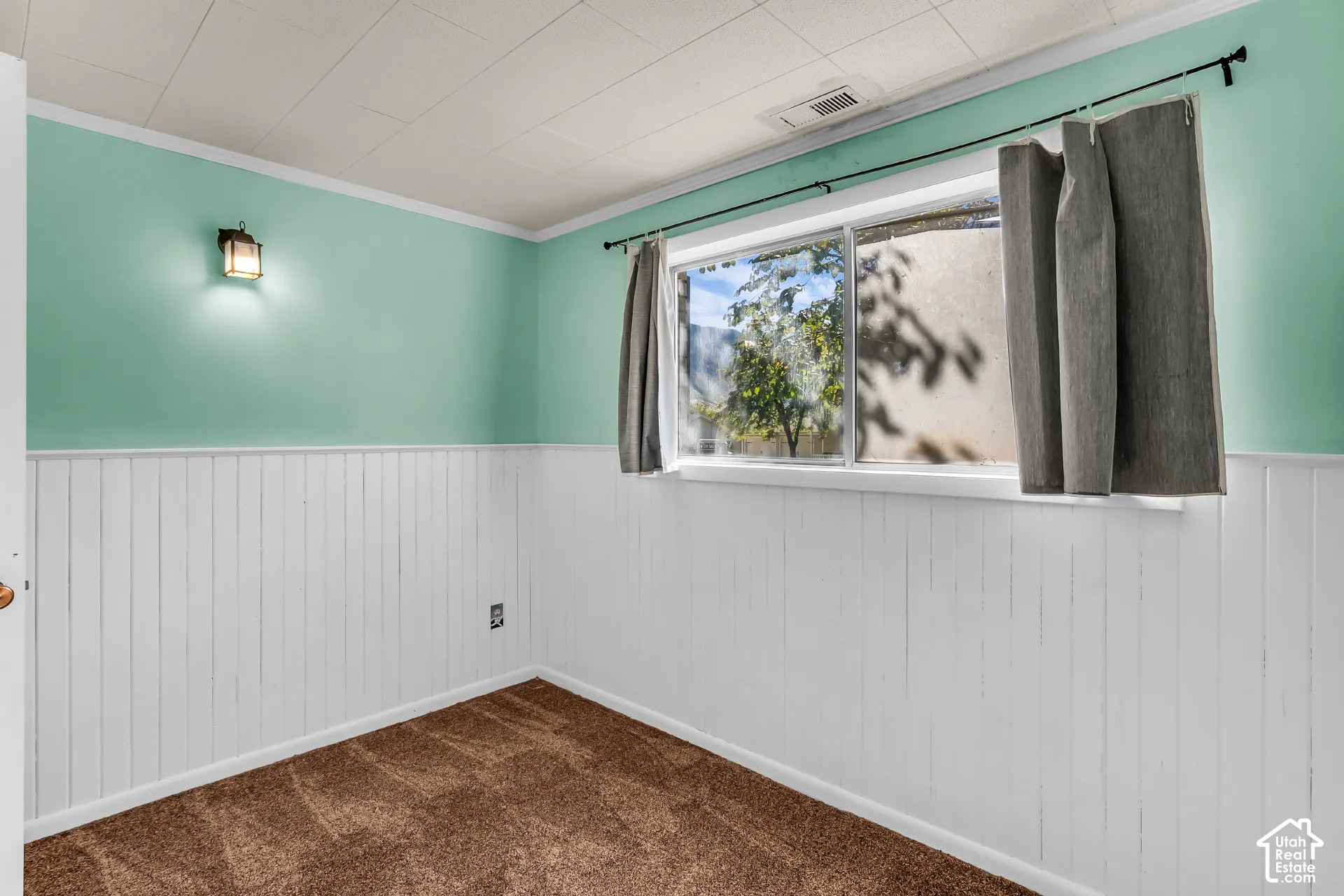 Room interior featuring white vertical wainscoting, carpeted flooring, a horizontal sliding window, and a wall-mounted light fixture