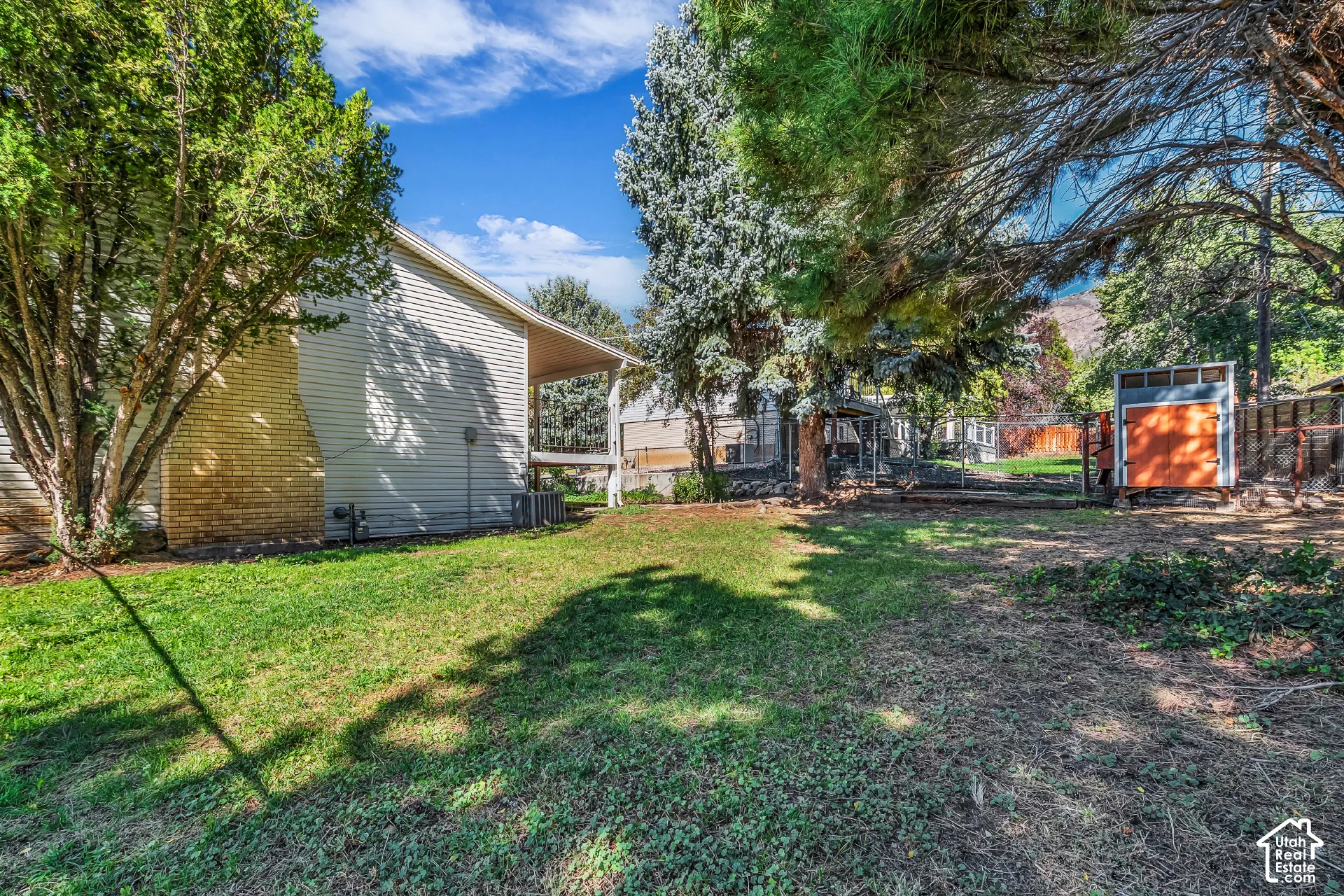 Side yard featuring horizontal siding, brick chimney detailing, covered patio space, and mature trees