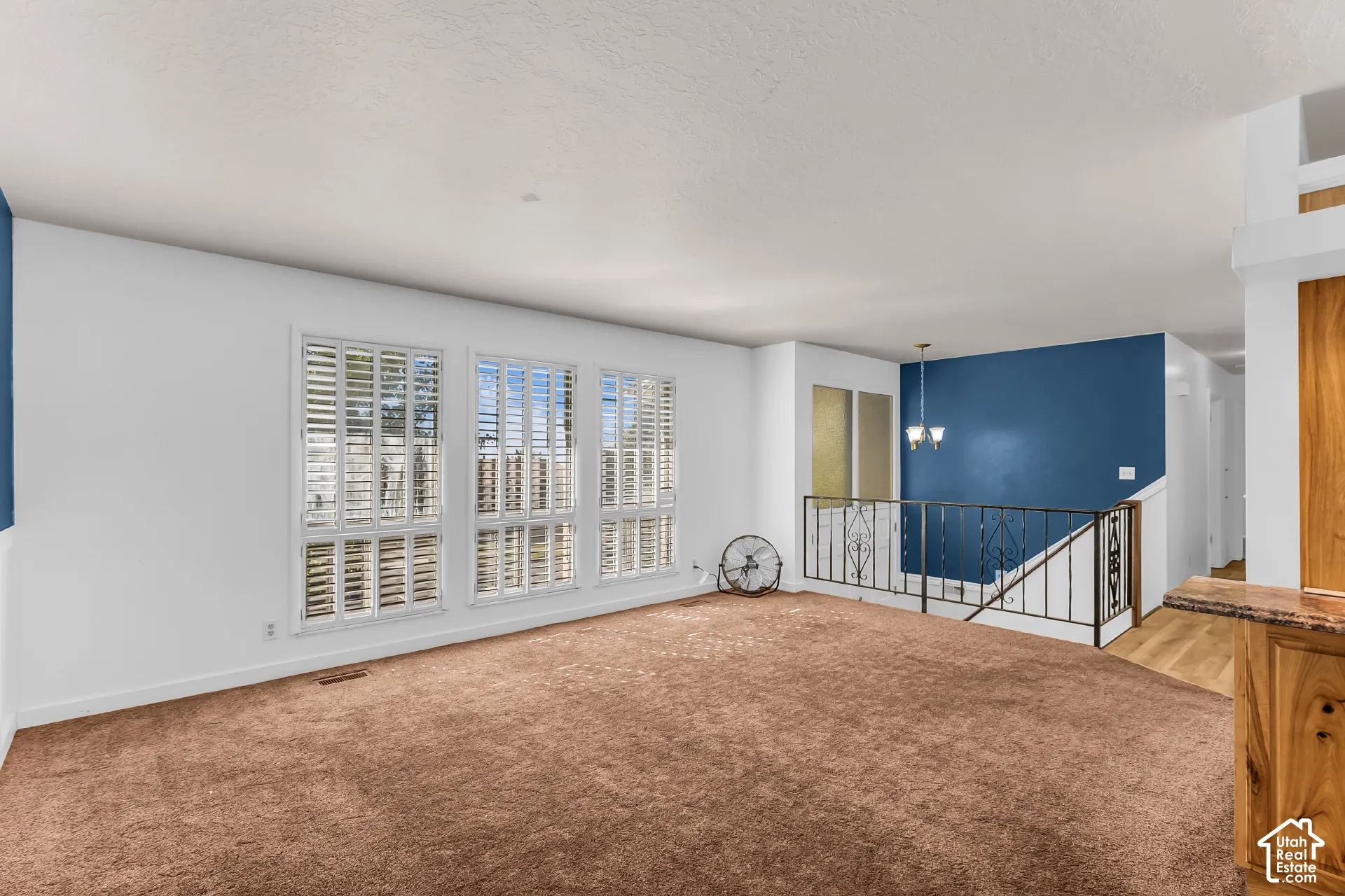 Living space featuring large windows with interior shutters, wrought iron stair railing, and accent wall paint