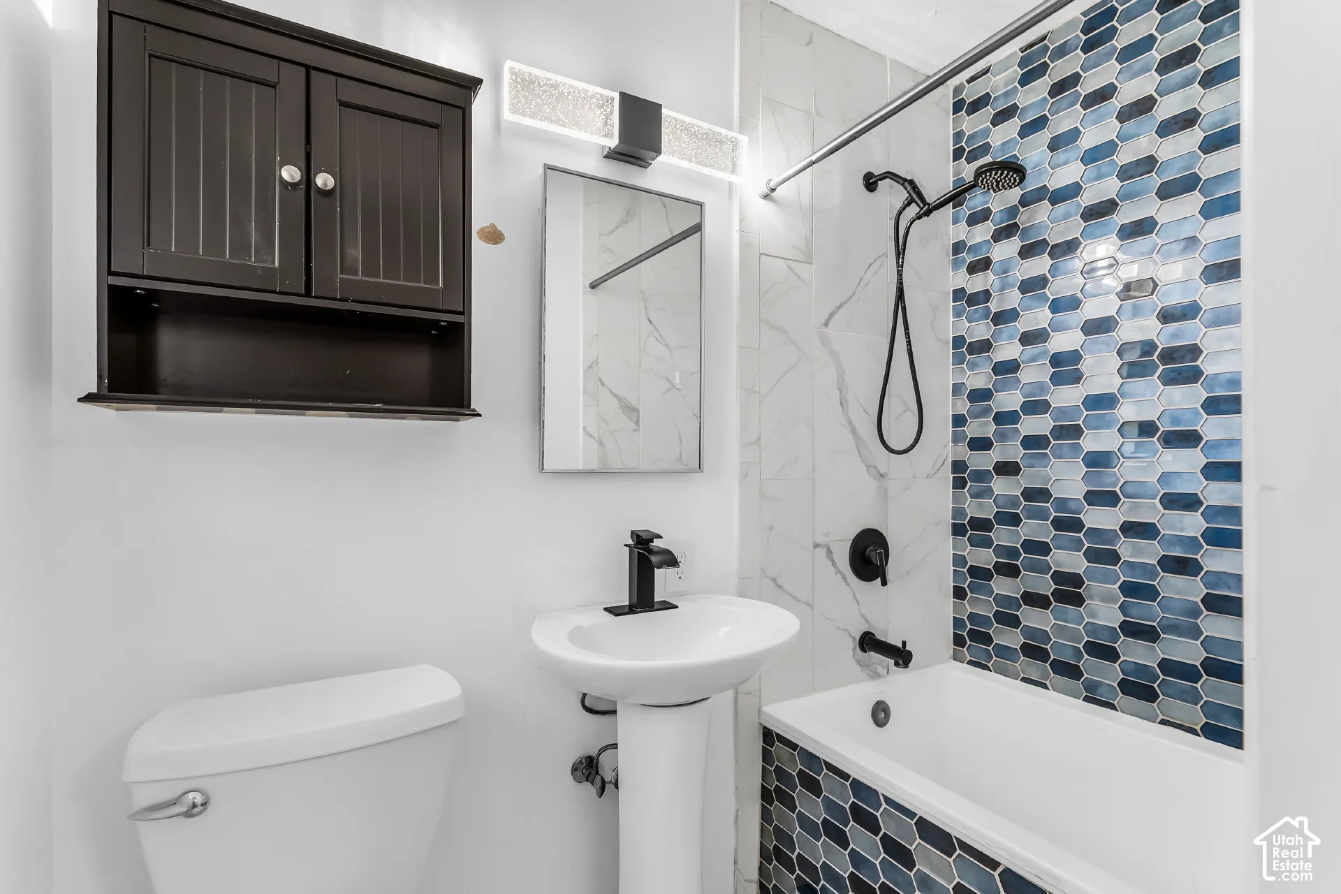 Bathroom featuring a pedestal sink, matte black plumbing fixtures, built-in wall cabinetry, and a shower-tub combination with blue and white multi-tone tile accents