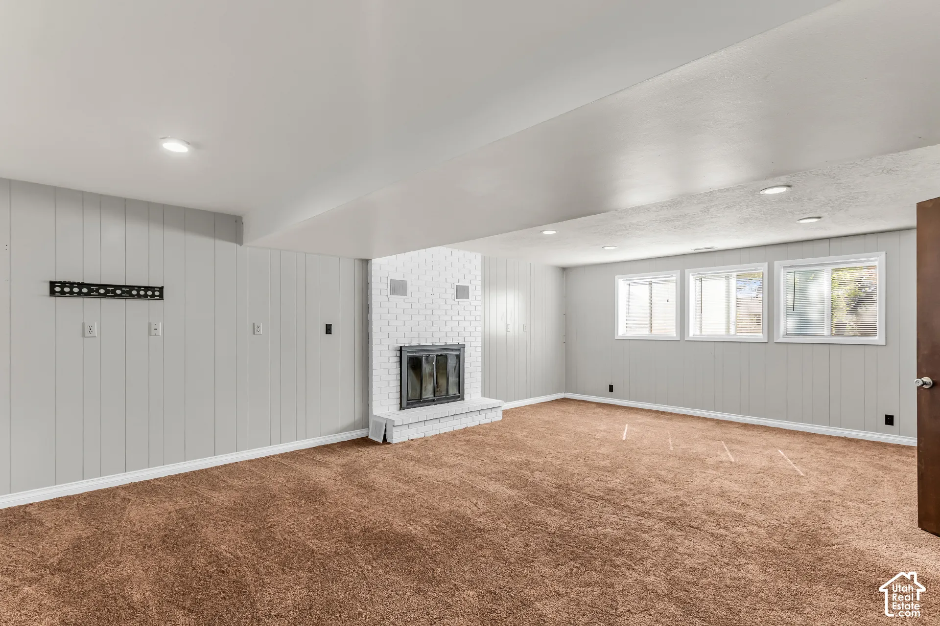 Interior space featuring light gray paneling, a white painted brick fireplace with a glass-front insert, carpeted flooring, and recessed ceiling lighting