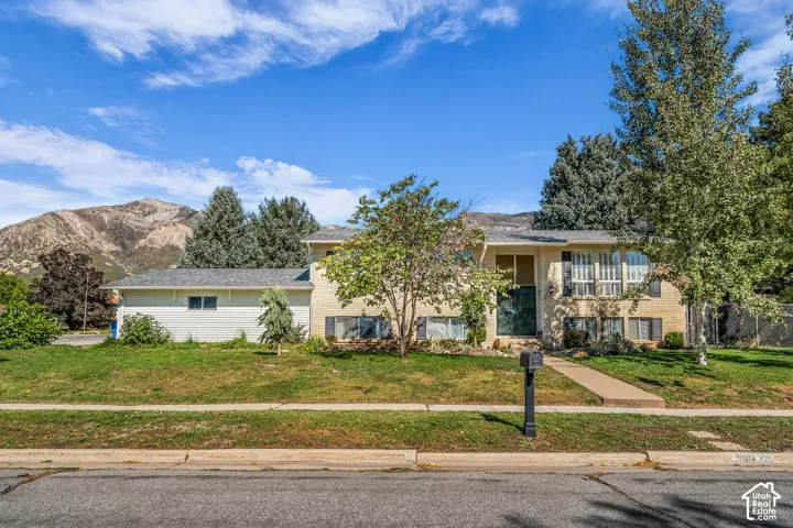 Exterior featuring light-toned brick and horizontal siding, mountain backdrop, mature trees, and a concrete walkway