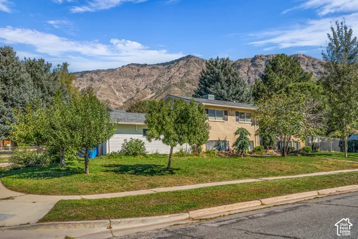 Split-level exterior featuring light brick and horizontal siding, set against a backdrop of mountain scenery, complemented by mature trees and a manicured lawn