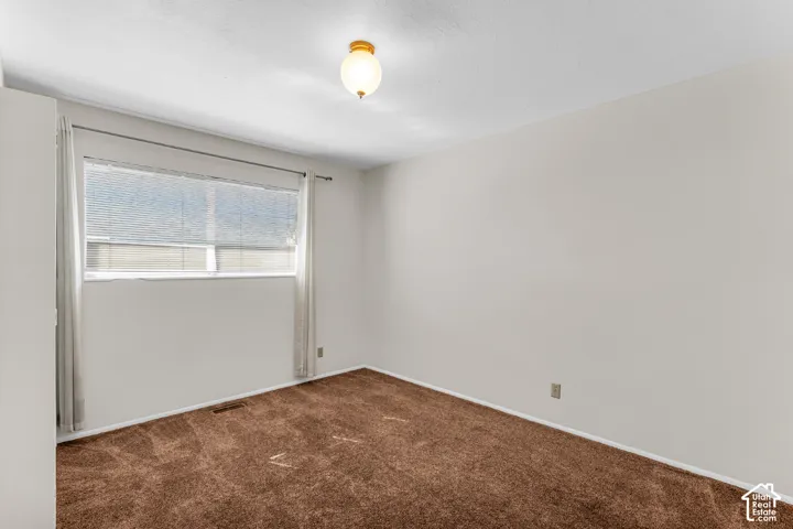 Neutral-toned interior room featuring brown carpeting, a horizontal sliding window, and a globe-style ceiling fixture