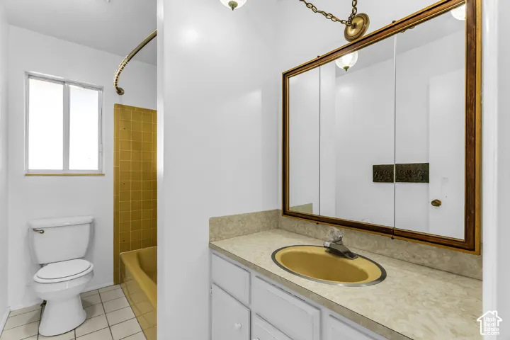 Bathroom featuring a vanity with integrated sink, stone-finish countertop, large wall-mounted medicine cabinet with gold-tone frame, shower-tub combination with yellow tile surround, and tile flooring