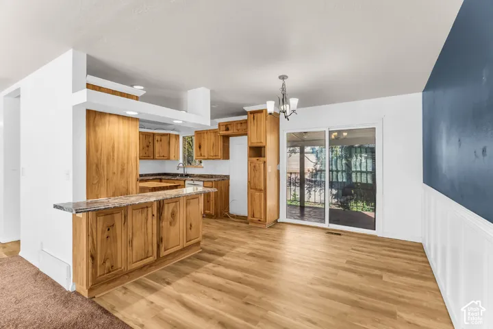 Kitchen featuring wood cabinetry, stone-finish countertops, wood-finish flooring, sliding glass patio doors, and wainscoting