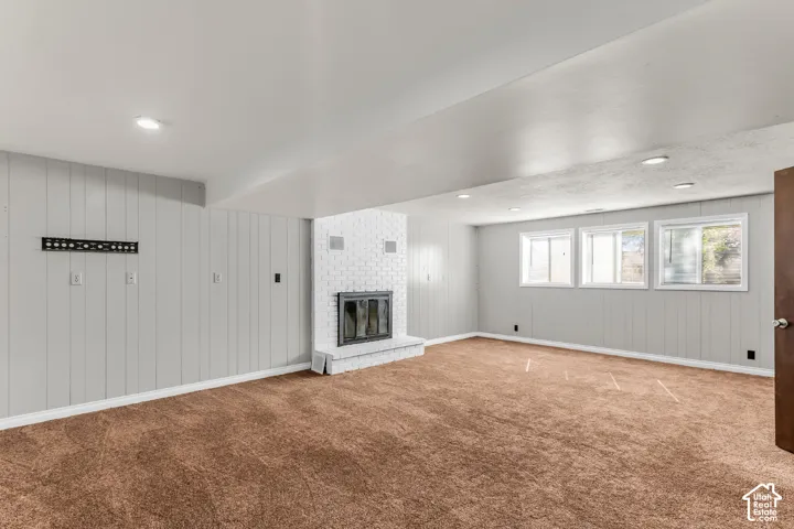Interior space featuring light gray paneling, a white painted brick fireplace with a glass-front insert, carpeted flooring, and recessed ceiling lighting