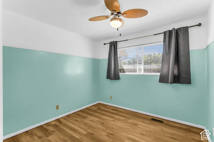 Room featuring wood-finish flooring, half-wall paint detailing, a sliding window with horizontal blinds, and a multi-blade ceiling fan with an integrated light fixture