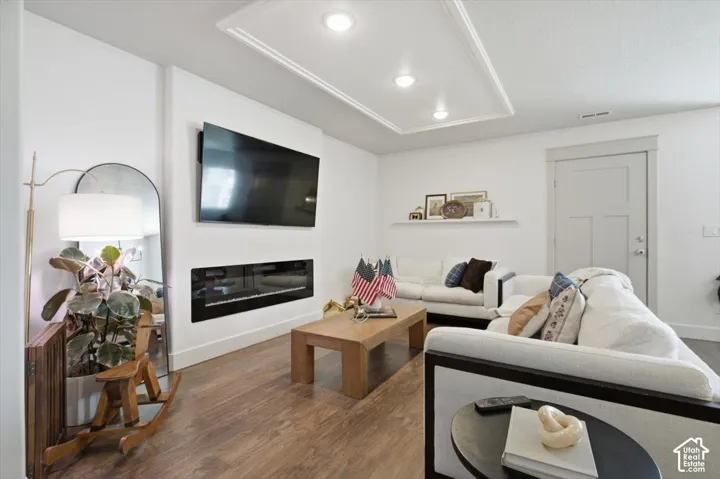 Living area featuring wood-finish flooring, recessed lighting with tray ceiling detail, a wall-mounted linear fireplace