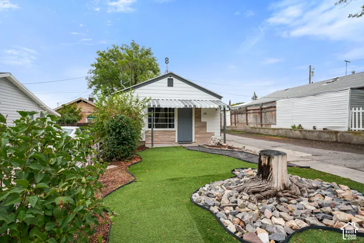 Exterior featuring white horizontal siding, stone-patterned accent wall, metal window awning, and landscaped lawn with stone ground cover