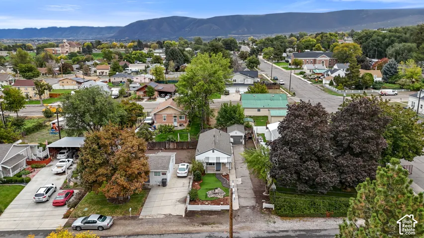 Aerial perspective of a single-story residence featuring a detached garage, concrete driveway, and front yard landscaping with a mountain backdrop