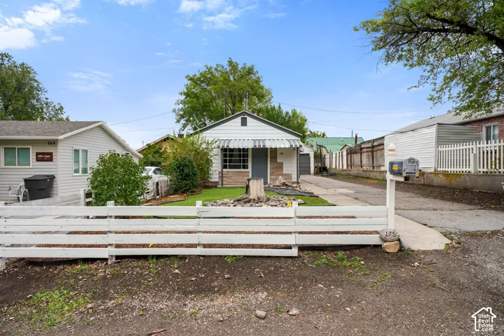 Single-story exterior featuring light-toned horizontal siding, a stone facade accent, metal awning over the entrance, and a white rail fence