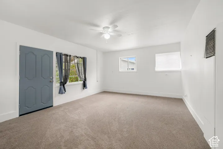 Neutral interior space featuring wall-to-wall carpeting, recessed ceiling fan with integrated lighting, dual-pane windows, and a paneled exterior entry door