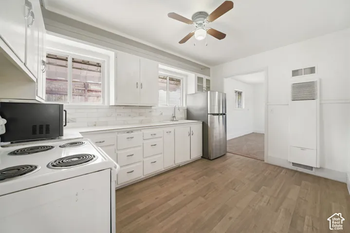 Kitchen featuring wood-finish flooring, white cabinetry, a stone-pattern backsplash, stainless steel refrigerator, and ceiling fan