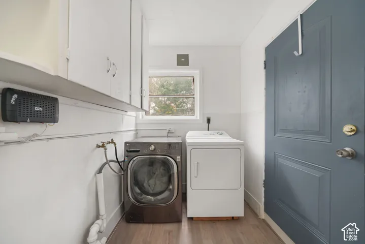 Laundry area featuring wood-finish flooring, white wall-mounted cabinetry, and a solid-core painted door
