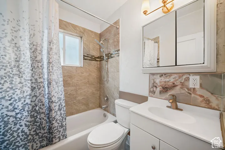 Bathroom featuring a tub-shower combination with floor-to-ceiling tile surround, decorative glass tile inlay, white cabinetry with integrated sink, and an above-mirror light fixture