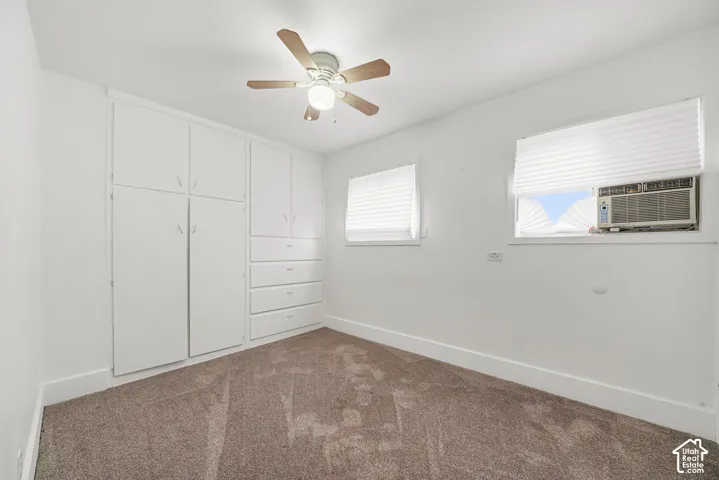 Bedroom featuring wall-to-wall carpeting, floor-to-ceiling built-in cabinetry with integrated drawers, a ceiling fan with light fixture, and windows with pleated shades