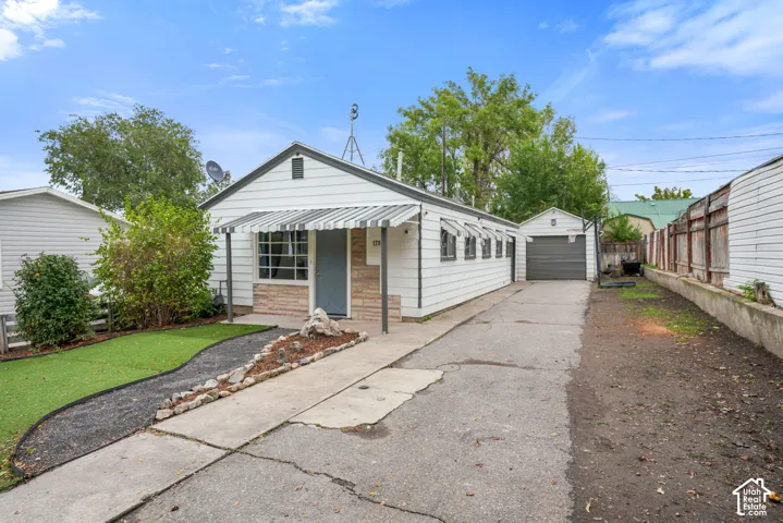 Single-story residence featuring white horizontal siding, stone veneer accents, striped metal awnings, a concrete driveway, and a detached garage
