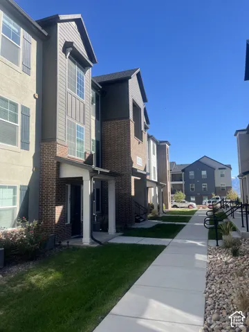 Multi-story residential exterior featuring a mixed-material facade of brick veneer, stucco, and vertical siding, complemented by gabled rooflines, decorative shutters, and concrete walkways