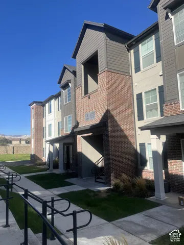 Multi-story exterior featuring a combination of brick masonry and horizontal siding, accented by dark shutter detailing, covered entryway, and concrete walkway