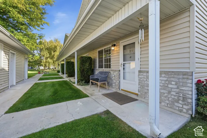 Exterior facade featuring horizontal siding and brick masonry, covered concrete porch, and concrete walkway flanked by manicured turf