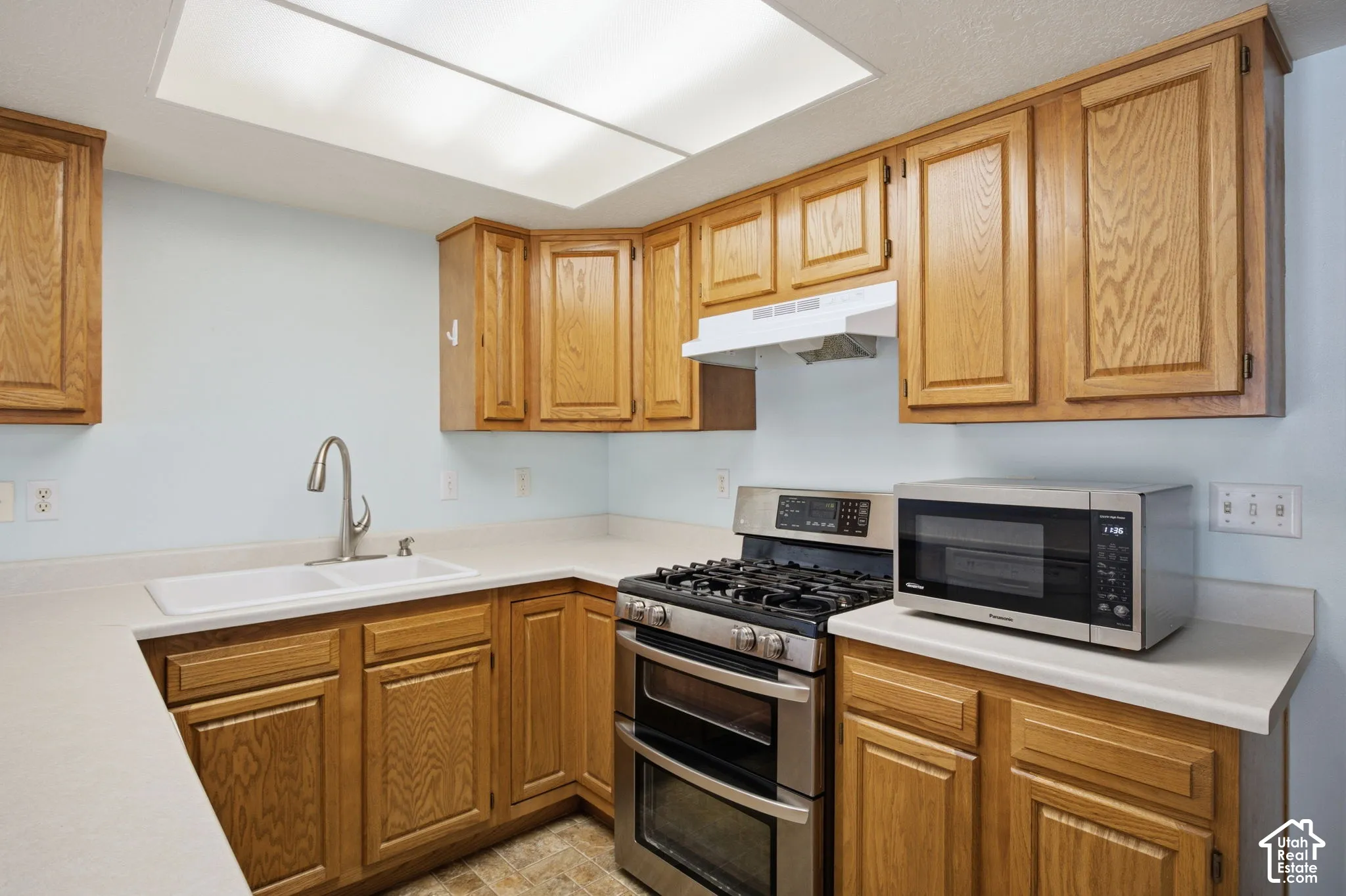 Kitchen featuring wood cabinetry, solid-surface countertops, dual-basin sink with high-arc faucet, and stainless steel gas range
