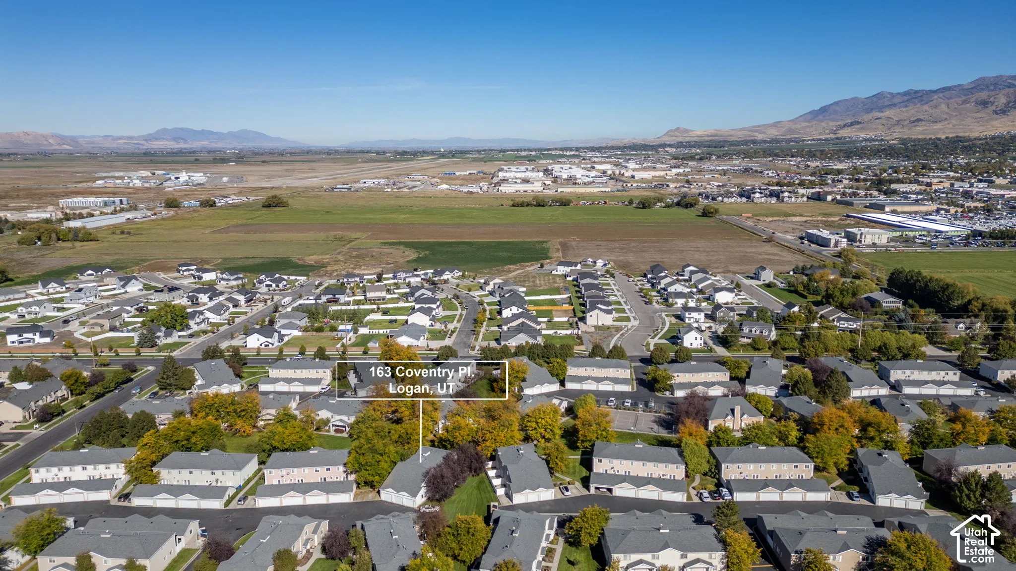 Aerial perspective of residential community featuring multi-unit housing, paved access roads, mature trees, and mountainous terrain in the distance